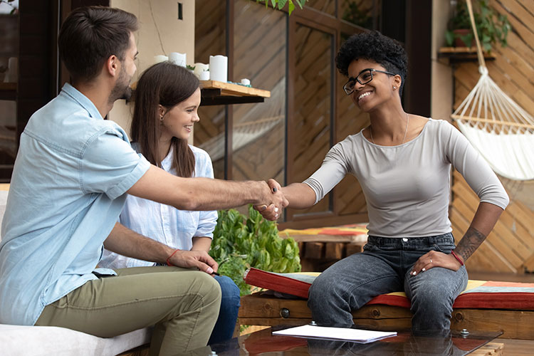 couple smiling and shaking hands with a woman who has papers in front of her