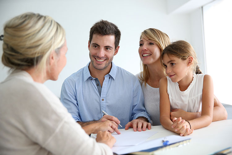 family smiling at a woman in a suit and signing papers