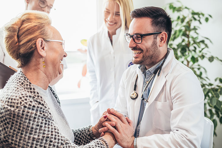 woman smiling happily at her doctor who is grasping her hands and smiling back