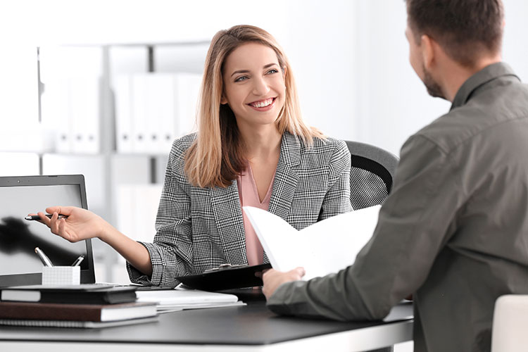 businesswoman with pen in hand smiling at colleague at her office desk